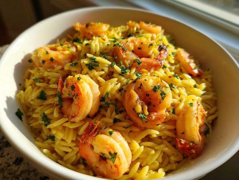 A close-up of a white bowl filled with bright yellow Lemon Garlic Shrimp Orzo, topped with cooked shrimp and fresh parsley.
