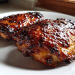 Close-up of two perfectly cooked Sticky BBQ Chicken Thighs with Honey Glaze on a white plate.