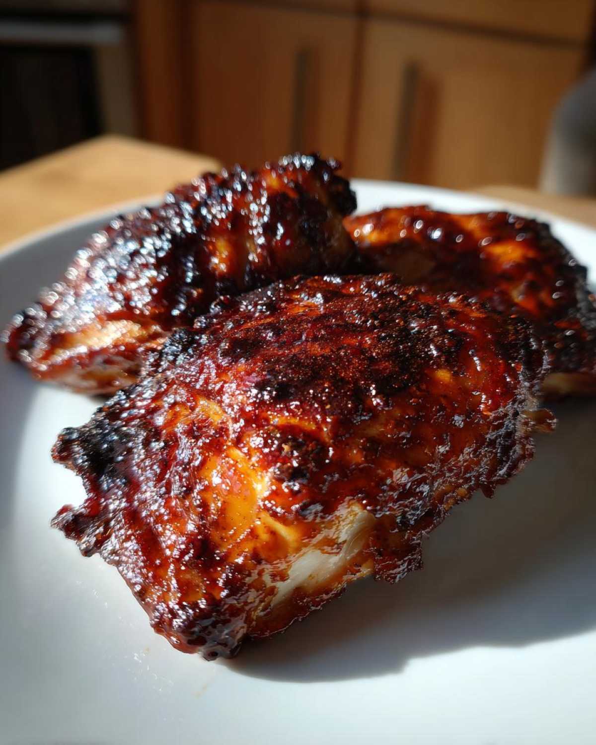 Close-up of three glistening, caramelized Sticky BBQ Chicken Thighs with Honey Glaze on a white plate.