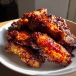 A pile of crispy oven Sticky BBQ Chicken Wings coated in a thick, glossy, dark red sauce.