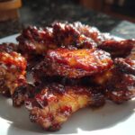 A close-up of several Sticky BBQ Chicken Wings Crispy Oven Style coated in a thick, glossy sauce on a white plate.
