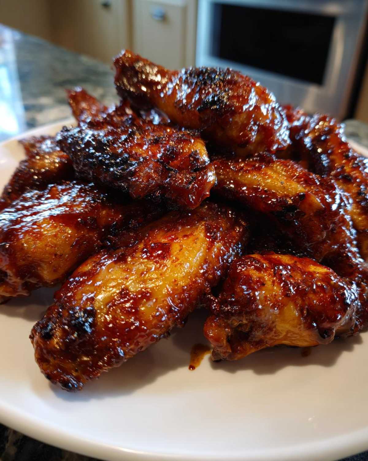 A pile of perfectly cooked Sticky BBQ Chicken Wings Crispy Oven Style glistening with sauce on a white plate.