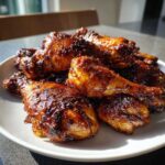 A close-up of several Sticky Honey Garlic Chicken Drumsticks Crispy piled high on a white plate.