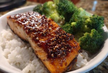 A perfectly cooked fillet of Sticky Honey Soy Salmon glazed with sauce and sesame seeds, served over white rice with steamed broccoli.
