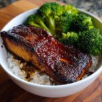 Close-up of a perfectly cooked Sticky Honey Soy Salmon fillet with a dark, glossy glaze served over white rice and steamed broccoli.