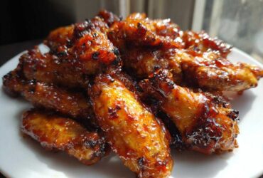 A pile of glistening, crispy Sticky Orange Chicken Wings Crispy Oven Style piled high on a white plate.