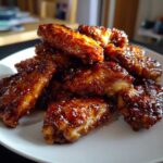 A pile of glistening Sticky Orange Chicken Wings with Honey Glaze sprinkled with sesame seeds on a white plate.