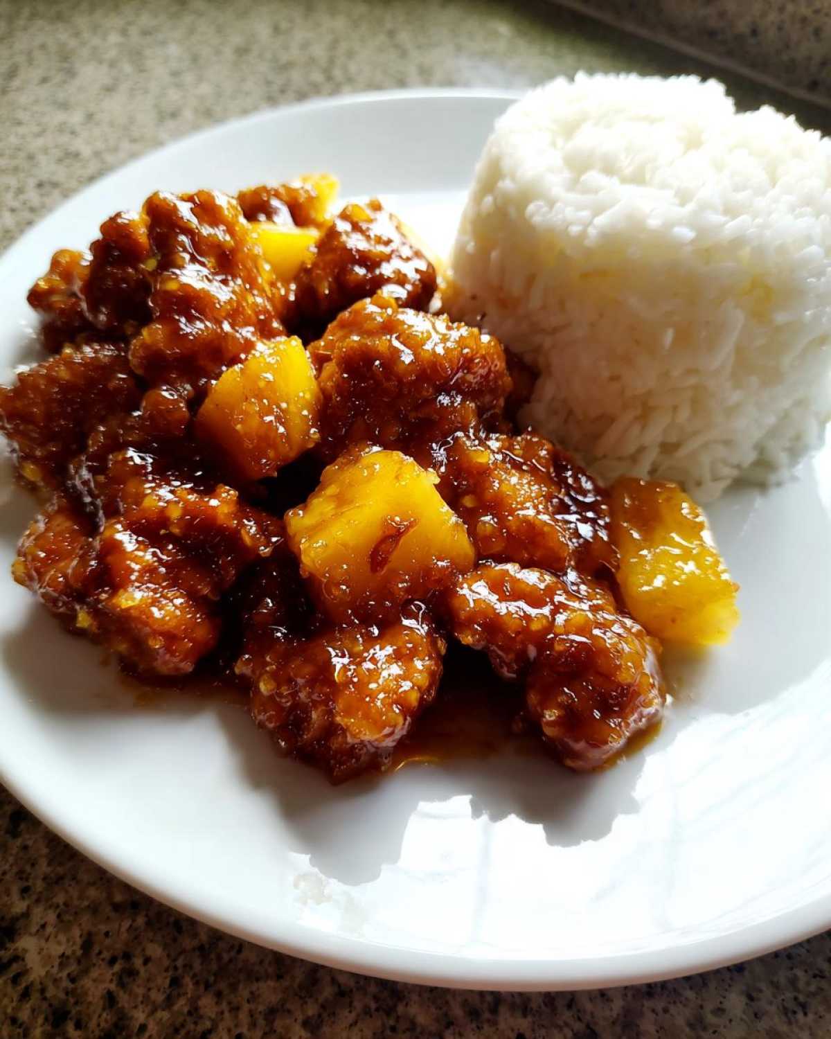 A plate of Sticky Pineapple Chicken with sweet glaze served next to a mound of white rice.