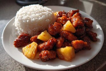 A plate of Sticky Pineapple Chicken with Sweet Glaze served next to a mound of white rice.