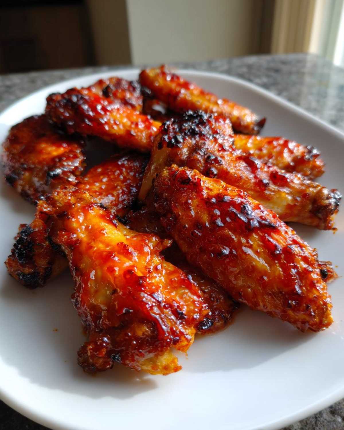 Close-up of glistening, caramelized Sticky Sweet Chili Chicken Wings Oven Baked piled on a white plate.