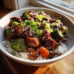 A close-up of a Sticky Teriyaki Chicken Bowl with rice, topped with glossy teriyaki sauce, broccoli, and green onions.
