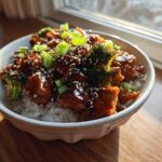 A close-up of a Sticky Teriyaki Chicken Bowl with rice, broccoli florets, and a sesame seed garnish.