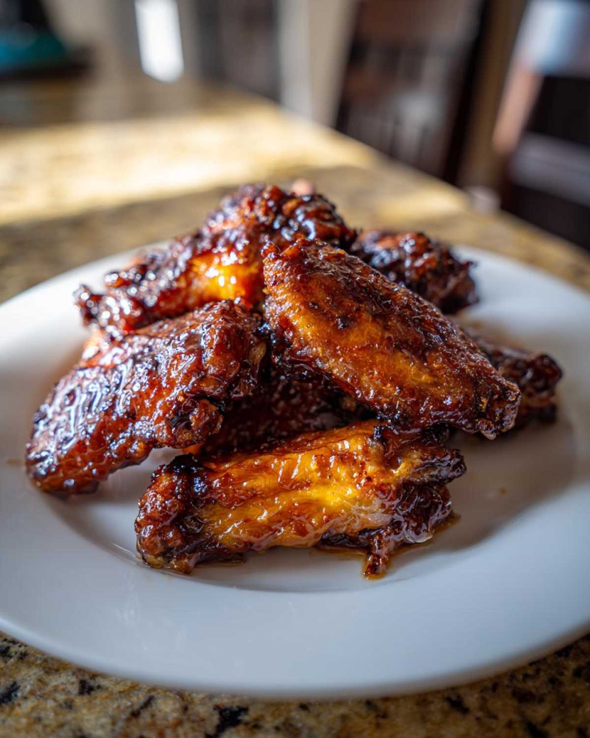 A close-up of oven baked Sticky Teriyaki Chicken Wings piled high on a white plate.