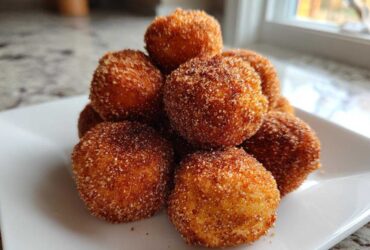 A stack of freshly fried Churro Bites coated generously in cinnamon sugar, served on a white square plate.