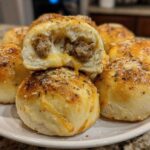 A plate piled high with golden brown pizza bombs, one cut open revealing melted cheese and sausage filling.