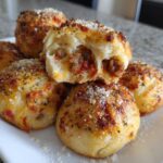 A stack of golden-brown pizza bombs, one cut open to show the savory sausage and sauce filling inside.