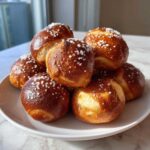 A stack of freshly baked, golden brown Pretzel Bites topped generously with coarse sea salt on a white plate.