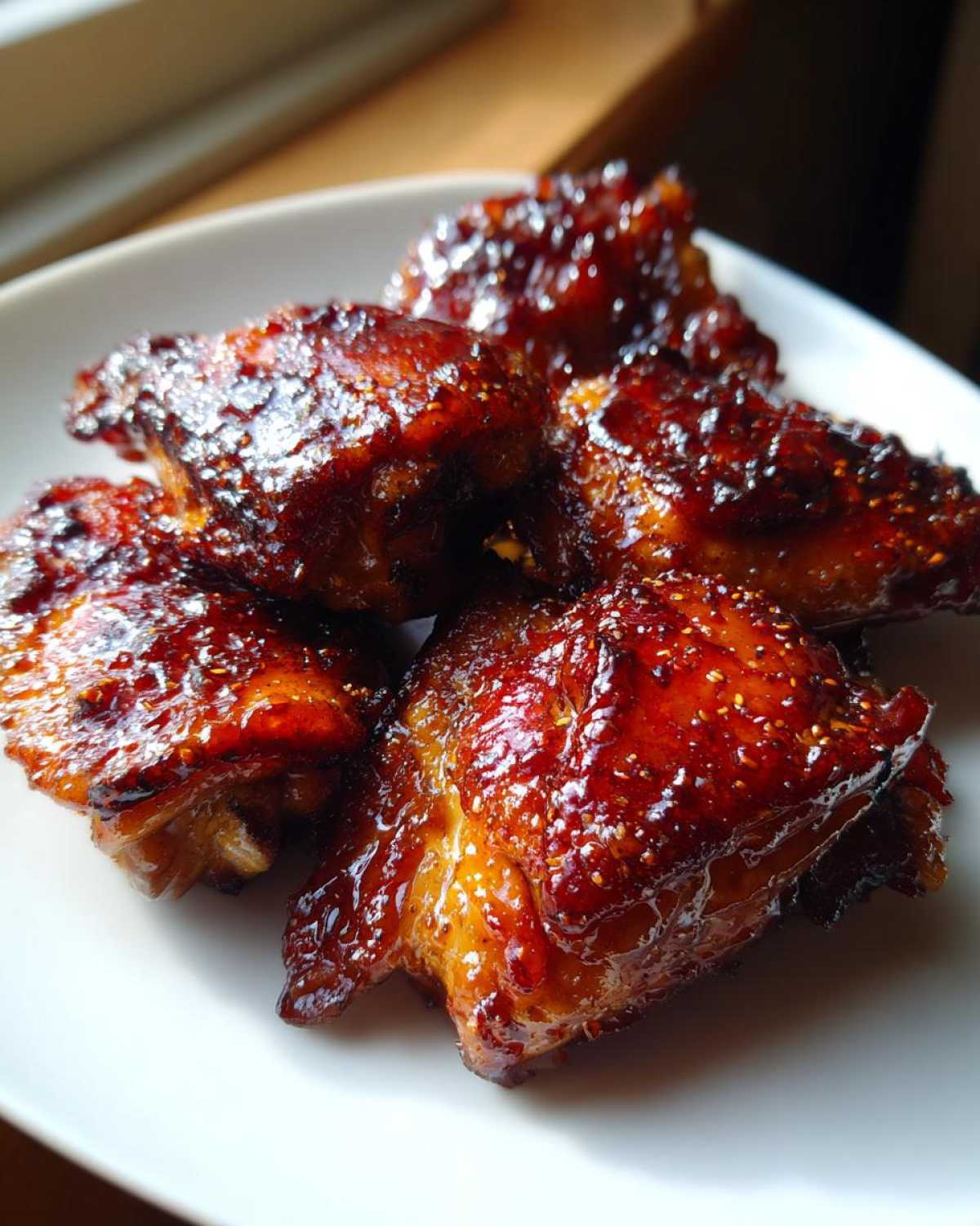 Close-up of several glossy, caramelized Baked Hot Honey Chicken wings piled on a white plate.