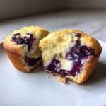 A close-up of a Blueberry Cream Cheese Muffin cut in half, showing the moist cake, burst blueberries, and creamy filling.