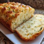A loaf of golden-brown Bread Machine Italian Herb Bread Loaded with Cheese and Garlic, with one slice cut and showing the soft interior.