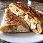 Two halves of a grilled Cheesy garlic chicken wraps showing juicy chicken chunks and melted cheese inside.