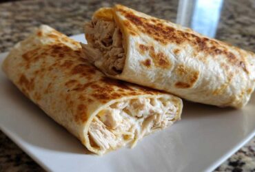 Two halves of a golden-brown Cheesy Garlic Chicken Wraps showing shredded chicken and creamy filling.
