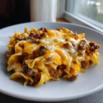 A close-up serving of Cheesy Hamburger Casserole featuring egg noodles, ground beef, and melted cheddar and white cheese.