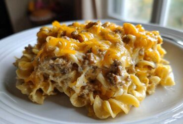 A generous serving of Cheesy Hamburger Casserole featuring ground beef, creamy sauce, and melted cheddar cheese over egg noodles.