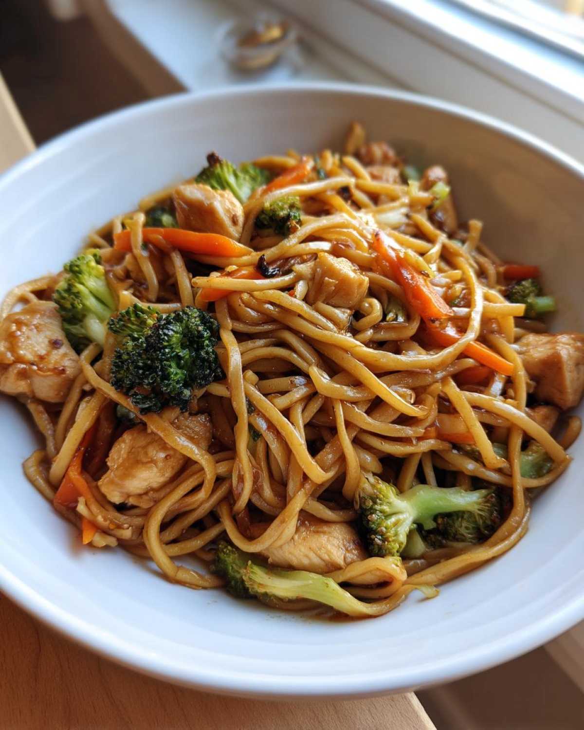 A close-up of chicken and broccoli Stir-Fried Noodles coated in a savory sauce, served in a white bowl.