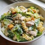Close-up of a bowl filled with Chicken Caesar Pasta Salad, featuring rotini pasta, romaine lettuce, chicken, and grated Parmesan.