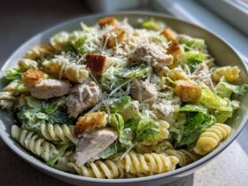A bowl filled with Chicken Caesar Pasta Salad featuring rotini pasta, grilled chicken pieces, romaine lettuce, croutons, and grated Parmesan cheese.