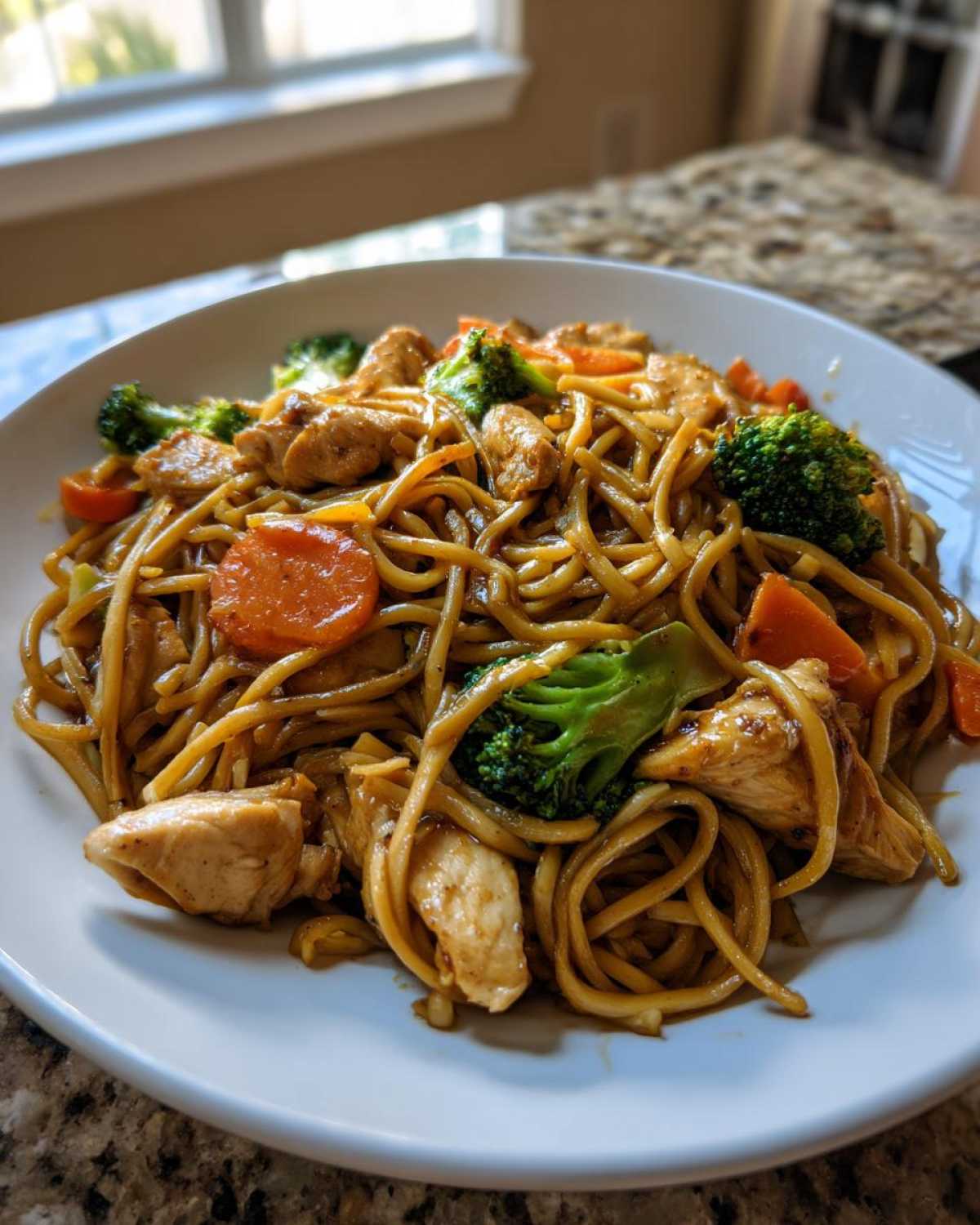 Close-up of a white bowl filled with savory Stir-Fried Noodles, chicken pieces, broccoli florets, and sliced carrots.