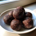A pile of dark, rich Chocolate Brownie Protein Balls speckled with seeds, served on a small white dish.