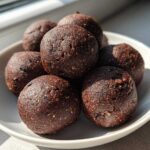 A close-up of several rich, dark Chocolate Brownie Protein Balls stacked in a small white bowl.