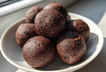 A close-up of several rich, dark Chocolate Brownie Protein Balls stacked in a small white bowl.