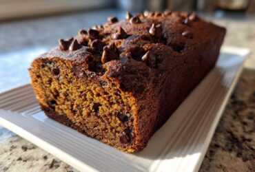 A close-up of a freshly baked Chocolate Chip Vegan Banana Bread loaf topped with melted chocolate chips.