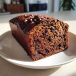 A moist slice of Chocolate Chip Vegan Banana Bread, rich brown in color, sitting on a white plate.