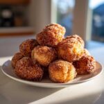 A tempting pile of freshly made Churro Bites coated in cinnamon sugar, stacked on a white plate.
