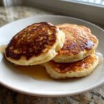 A stack of three fluffy Cottage Cheese Pancakes, perfectly golden brown and drizzled with syrup on a white plate.