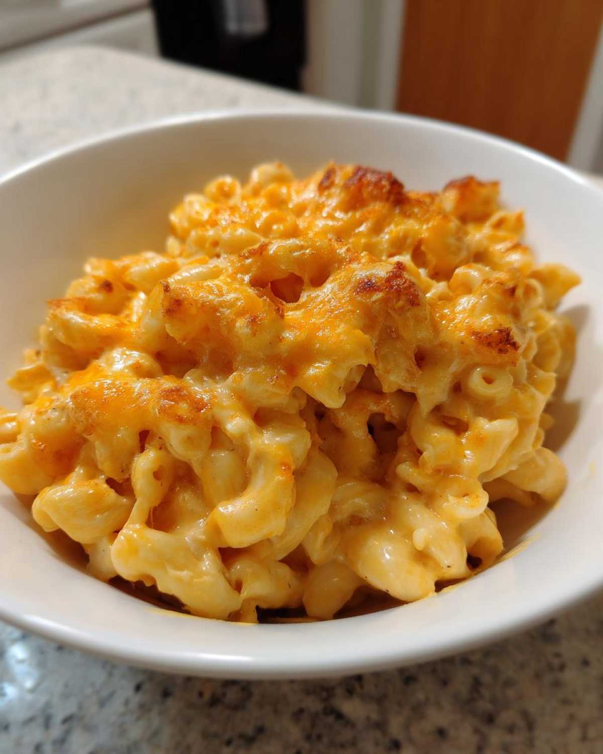 A close-up view of creamy, baked Chick-fil-A Mac and Cheese served in a white bowl with a slightly browned cheese topping.