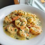A close-up view of plump shrimp coated in a rich, creamy garlic sauce and sprinkled with fresh parsley.