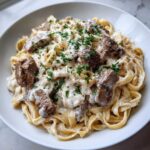 Close-up of a bowl filled with Creamy Steak Pasta Mouth Watering Protein Packed Meal with Garlic Boost, topped with parsley.