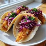Four Crispy Air Fryer Fish Tacos filled with golden fried fish and topped with vibrant red cabbage slaw.