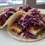 Three Crispy Air Fryer Fish Tacos topped with bright purple chipotle slaw on a white plate.