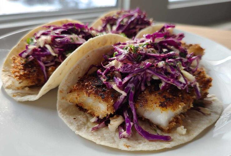 Three Crispy Air Fryer Fish Tacos topped with bright purple chipotle slaw on a white plate.