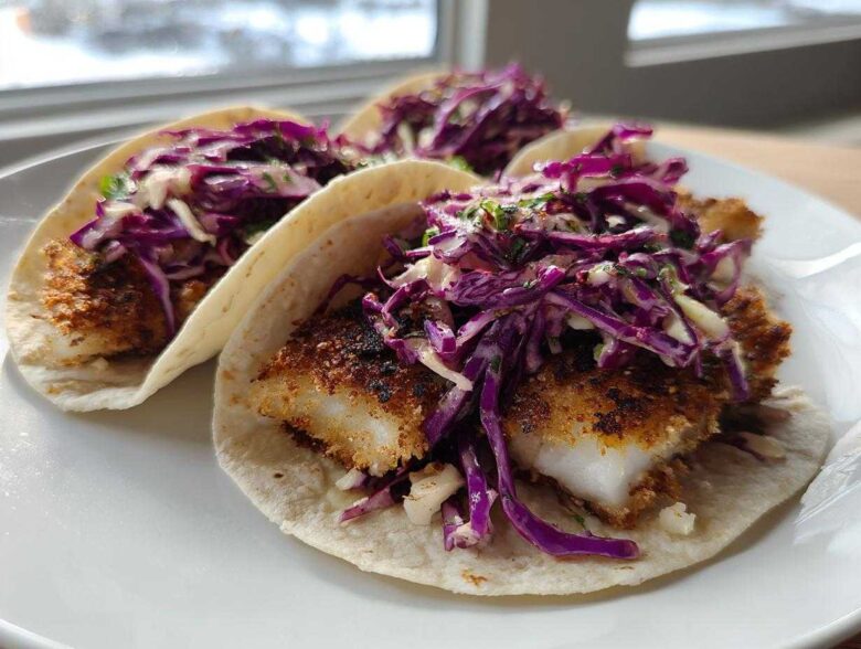 Three Crispy Air Fryer Fish Tacos topped with bright purple chipotle slaw on a white plate.