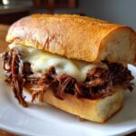 Close-up of a hearty Crockpot French Dip Sandwiches filled with shredded beef and melted white cheese on a crusty roll.
