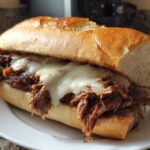 Close-up of a hearty Crockpot French Dip Sandwiches filled with shredded beef and melted white cheese on a toasted roll.