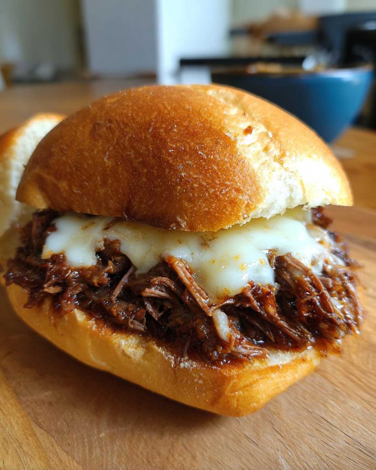 Close-up of a delicious Crockpot French Dip Sandwiches overflowing with shredded beef and melted white cheese on a toasted roll.