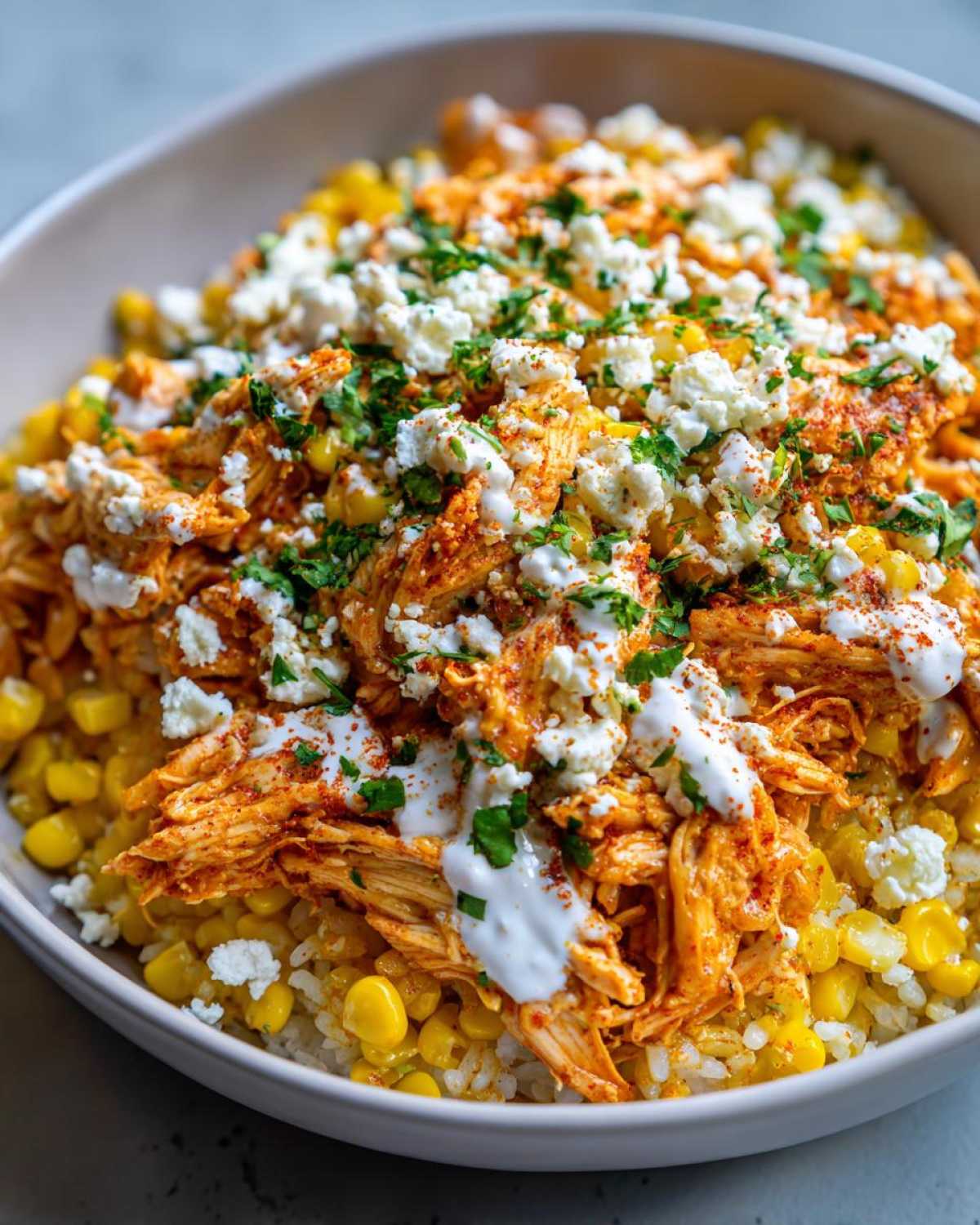 Close-up of a vibrant Flavor Street Corn Chicken Rice Bowl topped with crumbled cheese and crema.